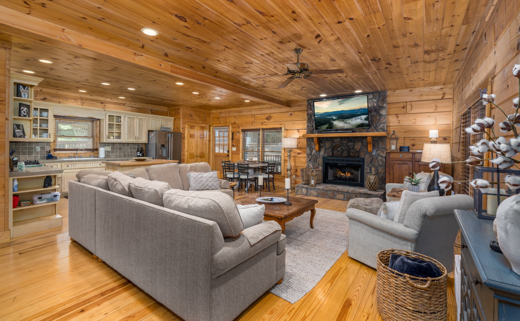 Open-concept living room, kitchen and dining with stone fireplace and pine walls