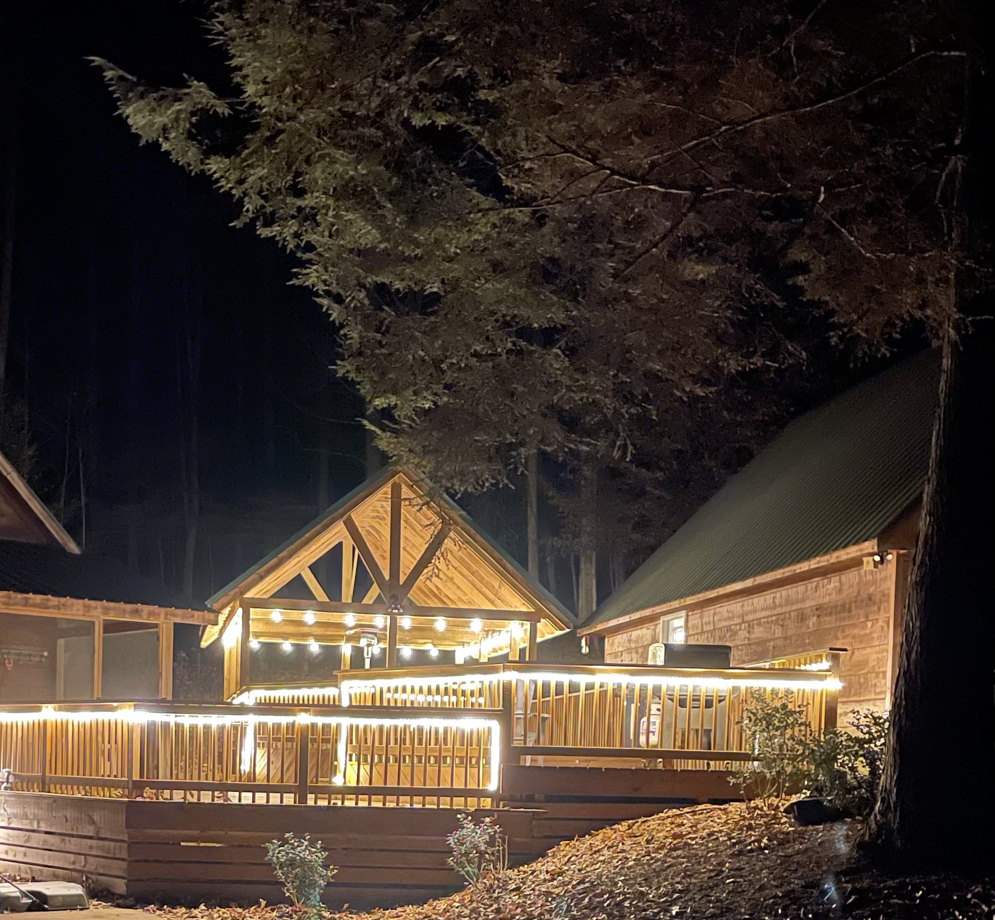 Cabin glowing at night with warm string lights on the deck and pavilion